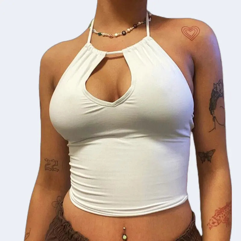 A young women wearing a white crop top, and necklace. white background, and tattooed arms.